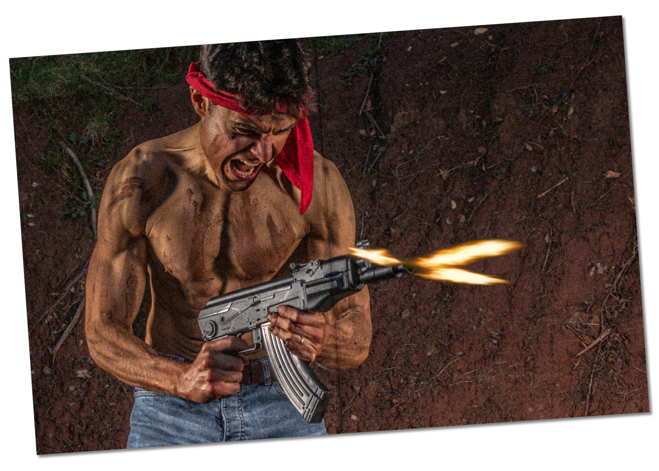 Ed Akay in Rambo-inspired shoot, standing shirtless with mud on his torso, wearing a red bandana, aiming and firing a compact Kalashnikov replica with visible muzzle flash, intense expression and tension in neck muscles, outdoors with mud bank and greenery in the background.