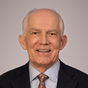 A professional looking gentleman, wearing a shirt, tie and blazer, is shown in a head and shoulders shot. He has a warm and approachable smile.