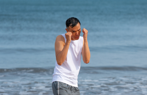 Male model training in Muay Thai stance on  shoreline