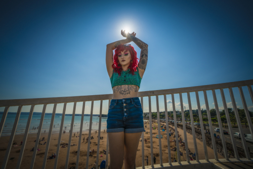 Female model with colourful hair poses against the railings with sun behind her at Torquay Beach - Jason Reading Photography