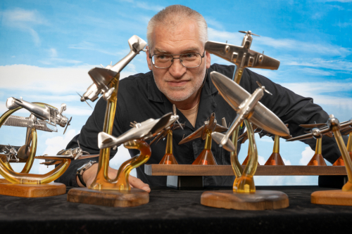 Robert Millis, aerospace engineer, leaning over and peering between his aluminium aerial combat sculptures, homage to Space: 1999.