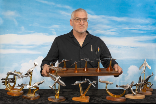 Third perspective of Robert Millis with aluminium aircraft sculptures against a blue sky, showing full display, and holding the Cold War six aircraft centrepiece sculpture in his hands.