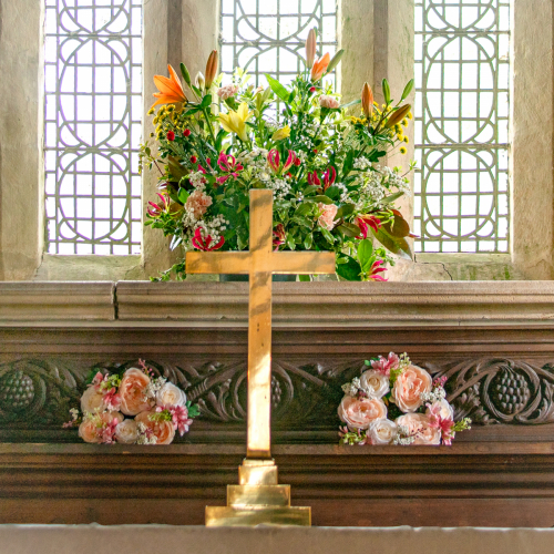 Wedding altar flowers in the window with cross at Wambrook Church