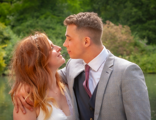 Bride and groom embrace and gaze at each other with the lake behind at Nine Springs, Yeovil
