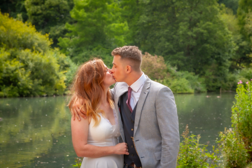 Wide shot of bride and groom kissing with lake in background at Nine Springs, Yeovil
