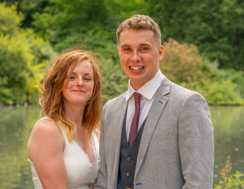 Close-up of bride and groom smiling at the camera by the lake at Nine Springs, Yeovil